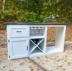 an outdoor bar with wine glasses and bottles on it's cabinet, in front of some trees