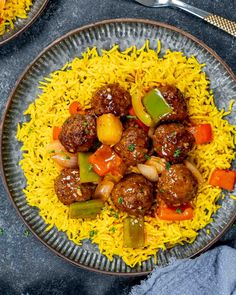 meatballs and vegetables over yellow rice on a plate with a fork next to it