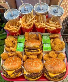 a table topped with lots of hamburgers and fries next to cups of soda on top of each other