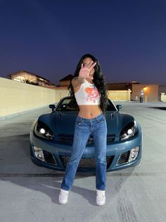 a woman standing in front of a sports car with her hand up to her face