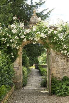 an archway with white flowers growing on it and stone walkway leading to the garden area