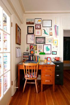 a wooden desk sitting under a window next to a wall filled with pictures and books