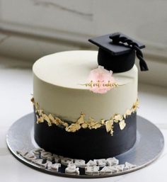 a white and black graduation cake with gold leaf decoration on top is sitting on a silver platter