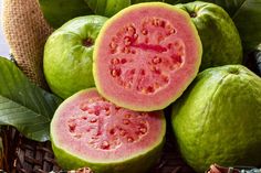 some green and red fruit sitting on top of each other in a basket next to leaves