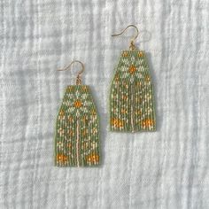 two pairs of green and yellow beaded earrings on a white cloth covered tablecloth