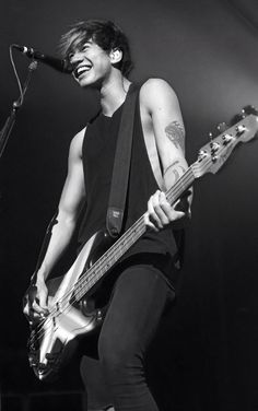 a young man playing a bass guitar in front of a microphone