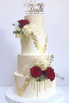 a three tiered wedding cake with red and white flowers on top is decorated with gold lettering