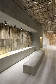 an empty room with benches and bamboo screens hanging from the ceiling, along with lights on either side of the wall