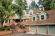 a large house with two garages in front of it and trees around the driveway