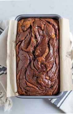 a loaf of chocolate banana bread in a pan on a white and blue towel with a striped napkin