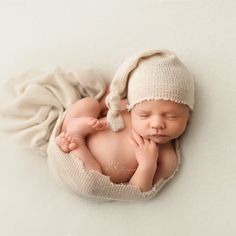 a newborn baby wearing a white hat and laying on it's side with his hands under his chin