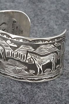 This sterling silver bracelet featuring horses grazing in a Southwestern landscape was made by Navajo silversmith Jeremy Delgarito. The back is signed J Delgarito and stamped sterling.Size: 5 3/8" (will fit up to a 6 3/4" wrist)Gap: 1 3/8"Width: 1 1/4"Free shipping on all orders! We ship with USPS and always include tracking. All orders ship within a day of payment.Returns are accepted up to 30 days after you receive your order. Just send us a message. Our shop offers cash back or store credit. Western Style Silver Bracelets For Gift, Western Sterling Silver Bracelet Stamped 925 As Gift, Western Style Silver Bracelet For Gift, Western Style Stamped 925 Bracelet As Gift, Western Style Engraved Bracelets For Gifts, Western Style Silver Bracelet Gift, Western Style Silver Engraved Bracelets, Silver Western Style Bracelet, Southwestern Etched Bracelets For Collectors