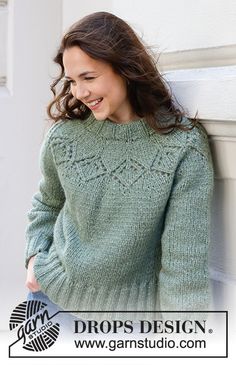 a woman leaning against a wall wearing a green sweater