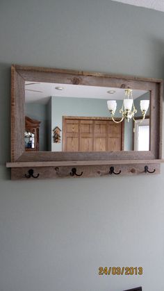 a mirror is hanging on the wall above a shelf with hooks and a chandelier