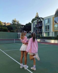 two girls standing on a tennis court with their arms around each other as they talk