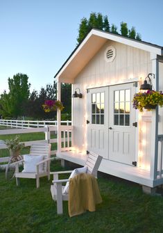 a small white shed with lights on the side and lawn furniture in front of it