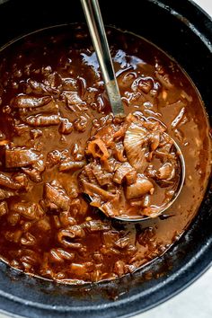 a ladle full of beef and beans in a slow cooker with a spoon