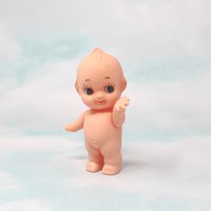 a small plastic baby doll standing up on a white surface with one hand in the air