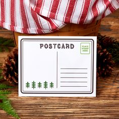 a postcard sitting on top of a wooden table next to pine cones and evergreen leaves