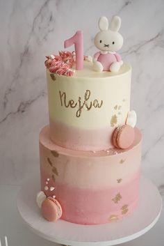 a pink and white two tiered cake with a teddy bear on top