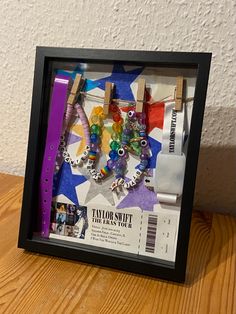 a shadow box with some beads and clothes pins in it on a wooden table next to a white wall