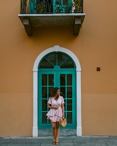 a woman standing in front of a green door with a pink dress and straw bag