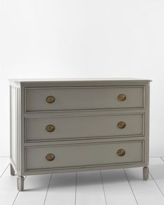 a white dresser with three drawers and gold handles on the bottom drawer, in an empty room