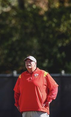 a man standing on top of a field wearing a red shirt and white pants with his hands in his pockets