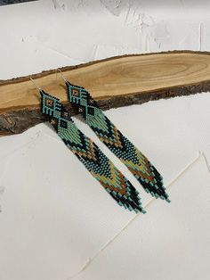 a pair of beaded earrings sitting on top of a piece of wood