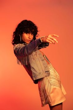 a woman in a short skirt and jean jacket is holding her hand out to the side