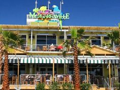 people are sitting at tables in front of a building with awnings and palm trees