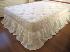 a white bed with ruffled bedskirt on the bottom and bottom layer, in front of a radiator