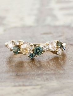 a gold ring with green and white stones on it's side, sitting on a wooden surface