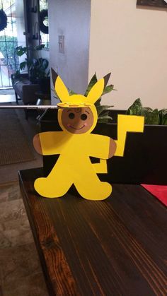 a paper cut out of a cartoon character sitting on top of a wooden table next to a potted plant