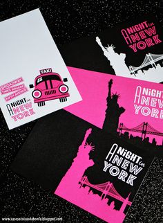 some pink and black business cards are laying on a table with the statue of liberty in the background