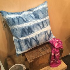 a blue and white pillow sitting on top of a wooden box next to a pink scarf