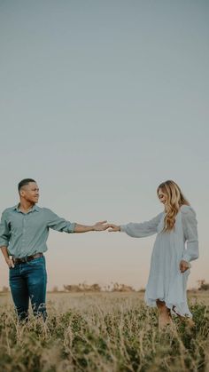 a man and woman holding hands while standing in the middle of a field with tall grass