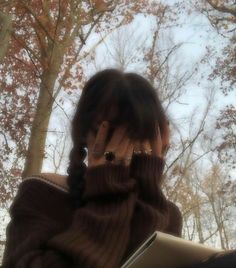 a woman covers her face with her hands while looking out the window at autumn trees