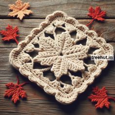 a crocheted doily with autumn leaves on the wooden table next to it