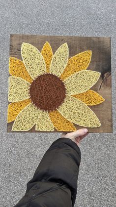 a person holding up a piece of string art with a sunflower on it's side