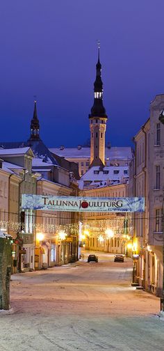 an empty city street at night with the lights on and clock tower in the background