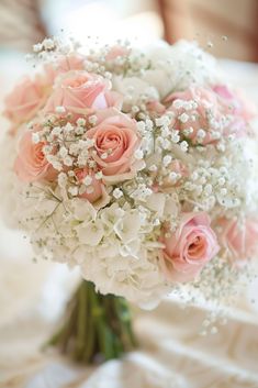 a bouquet of pink roses and baby's breath sits on a white tablecloth