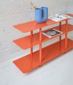 an orange table with two blue vases on top and a magazine rack below it