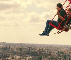 two men sitting in a red chair on top of a tall building over looking the city