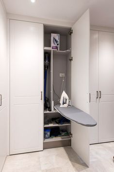 an ironing board is in the closet next to some white cupboards and cabinets