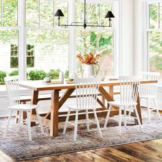 a dining room table with four chairs in front of large windows and an area rug on the floor