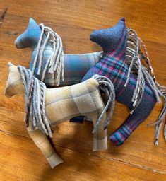 two small horses made out of fabric on a wooden floor, one is grey and the other is blue