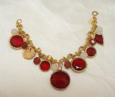 This vintage ruby red glass charm bracelet is truly a standout. The fifteen charm bracelet by Accessocraft is one of their best. The bracelet has faceted glass charms, glass beads, bicolor beads, and a faux Roman coin all attached to a unique goldtone bracelet. There are six faceted red glass charms in goldtone frames. There is a shield, two small rounds, two medium rounds and a large red glass charm. Each glass charm is flat on one side and pointed on the other. In addition there are four white Faberge Jewelry, Brass Cuff Bracelet, Roman Coins, Glass Charms, Copper Pendants, Faceted Glass, White Beads, Red Glass, Ruby Red