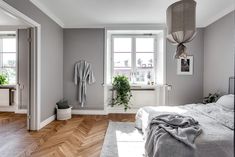 a bedroom with grey walls and wooden floors, white bedding and two plants on the window sill