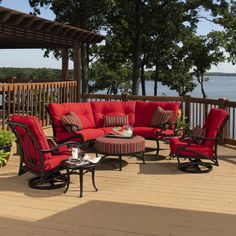 an outdoor patio with red cushions and furniture on the deck next to trees, overlooking water